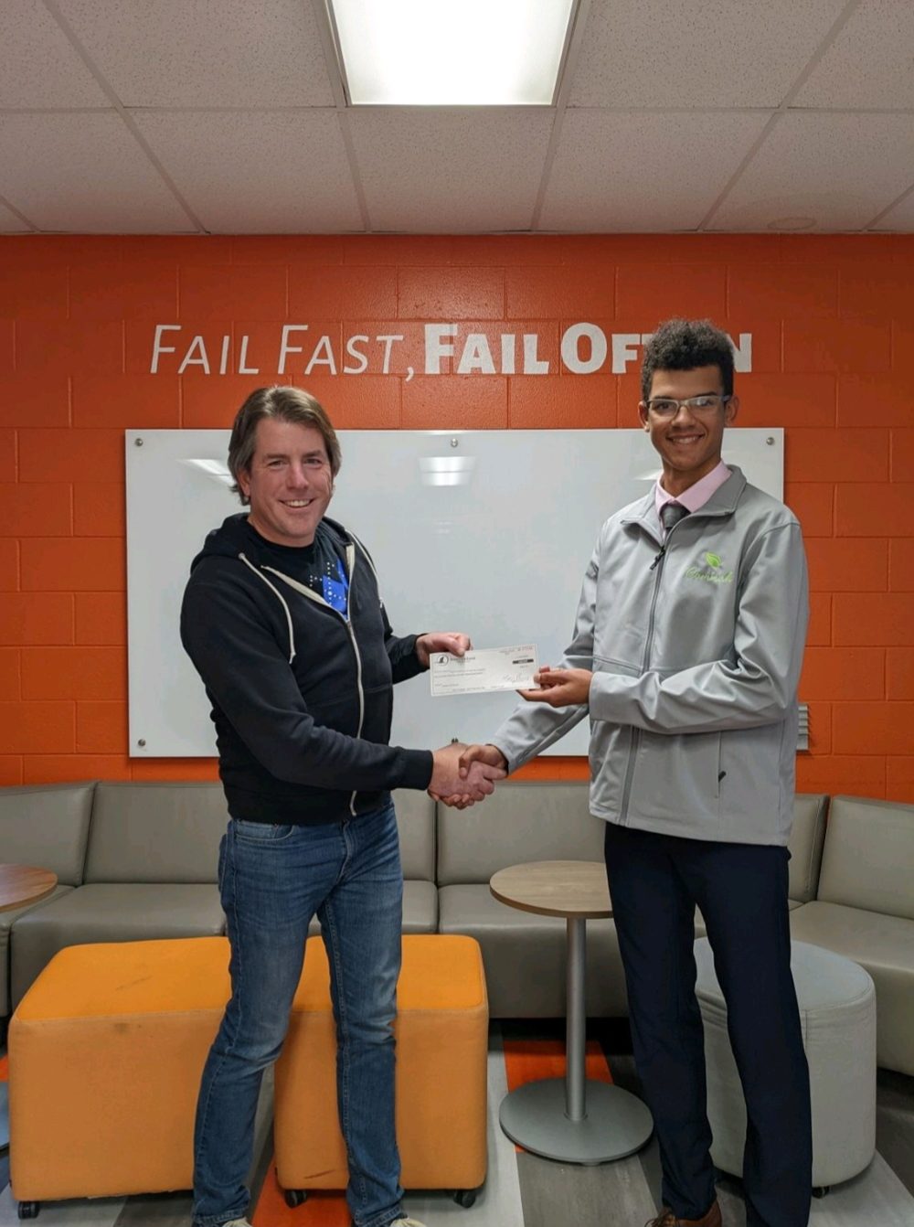 Ayden receiving a check in front of a Fail Fast Fail Often wall