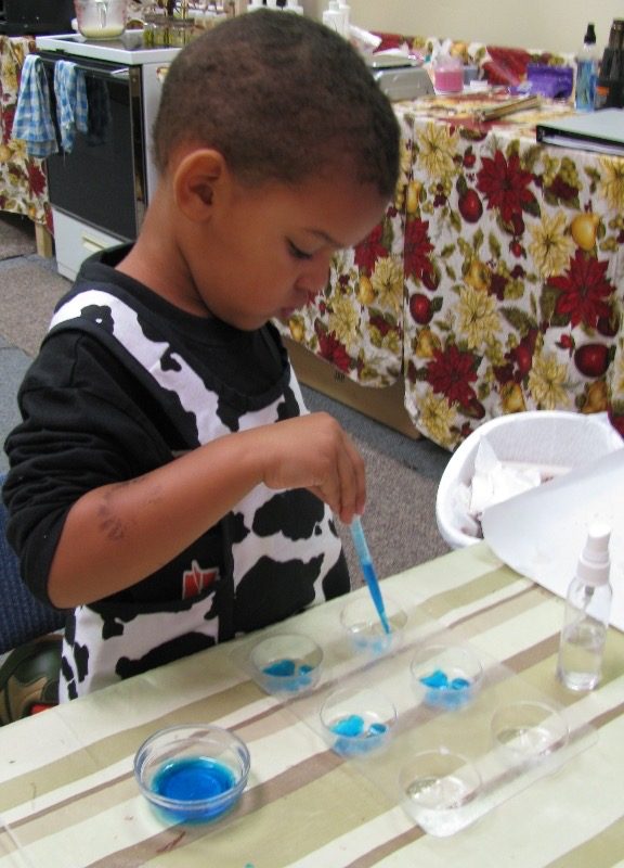 A very young Ayden mixing colors at a kitchen table